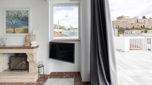 Un salón moderno con chimenea, televisor montado y vistas a ruinas antiguas.