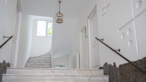 Una escalera de mármol con un candelabro, paredes blancas y vistas al exterior.