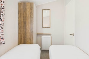 Una habitación pequeña y ordenada con dos camas, un panel de madera decorativo, un radiador y un espejo.