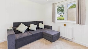 A modern living room with a grey sectional sofa, a white radiator, and a window with curtains.