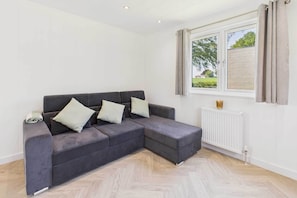 Ein modernes Wohnzimmer mit einem grauen Ecksofa, einem weißen Heizkörper und einem mit Vorhängen versehenen Fenster.