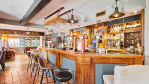 A bar area with wooden bar counter, stools, and shelves stocked with bottles.