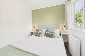 Ein Schlafzimmer mit einem Bett, zwei Nachttischen, einem Fenster mit Vorhängen und einer Heizung.