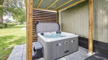 Un bain à remous sous une pergola en bois, avec une pelouse verdoyante en arrière-plan.