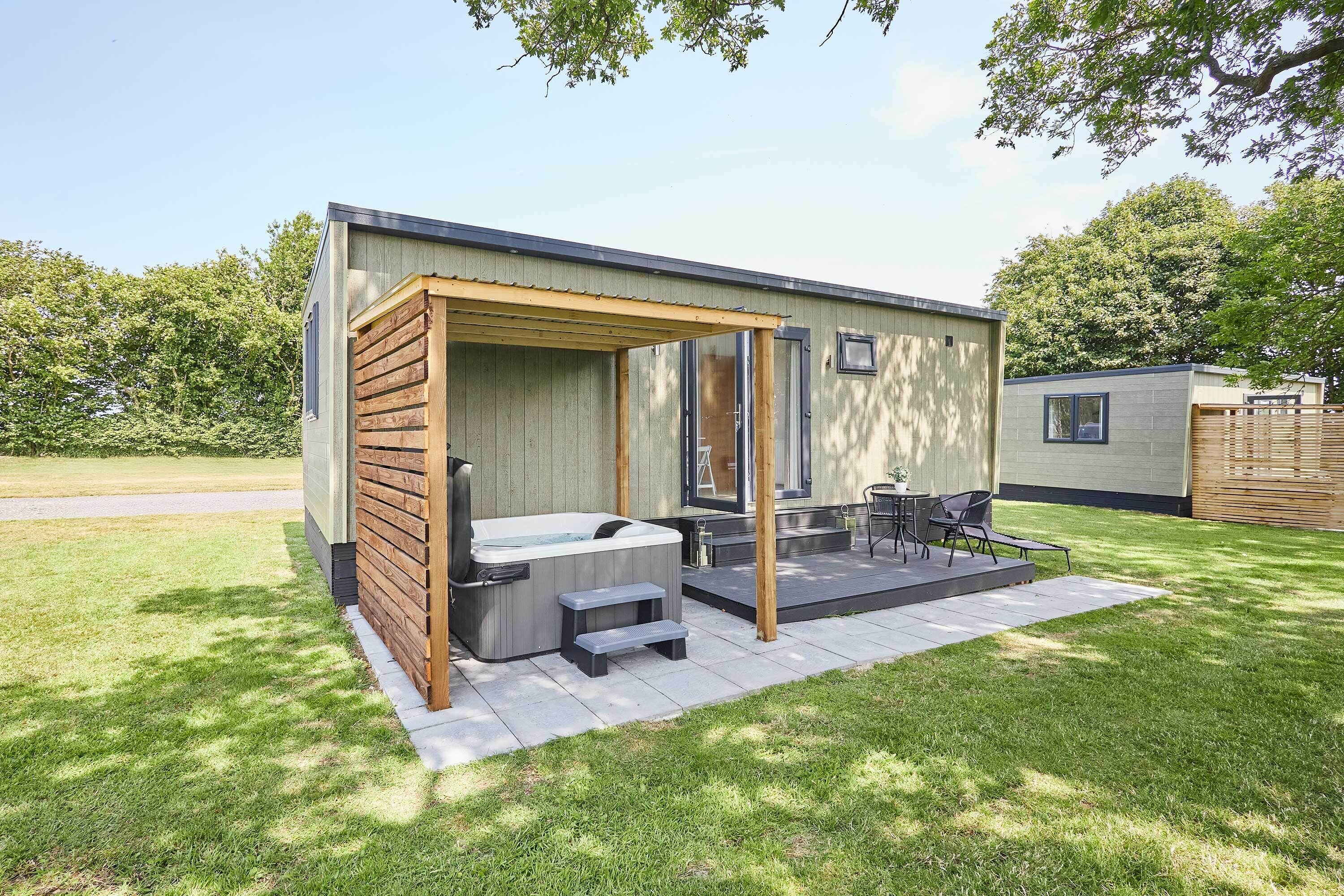 Un espace moderne aménagé à l’extérieur avec un bain à remous, une pergola en bois, un coin salon et une petite table.