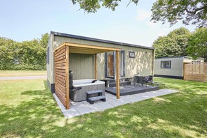Un espace moderne aménagé à l’extérieur avec un bain à remous, une pergola en bois, un coin salon et une petite table.