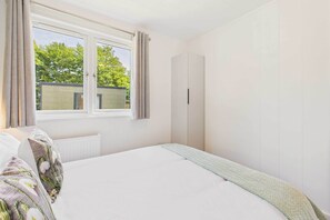 Un dormitorio con un ventanal grande, una cama con almohadas estampadas, un radiador y un armario.