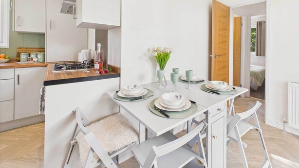 A modern kitchen with white cabinetry, a wooden countertop, and a dining area with white chairs and a table set for four.