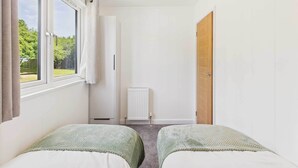 A bedroom with two beds, a window, a radiator, and a door.