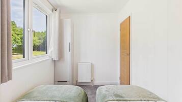 Une chambre avec deux lits, une fenêtre, un radiateur et une porte.