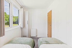 A bedroom with two beds, a window, a radiator, and a door.
