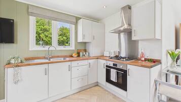 A modern kitchen with white cabinets, a stainless steel range hood, a built-in oven, and a window providing natural light.