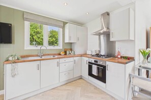 A modern kitchen with white cabinets, a stainless steel range hood, a built-in oven, and a window providing natural light. - Host & Stay | Pod 2 @ Kingsmoor Retreat (Coleorton)