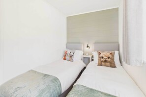 Quarto de hotel com duas camas de solteiro, cada uma com travesseiro e mesa de cabeceira com abajur.