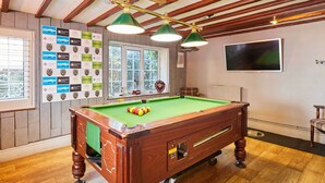 A pool table in a room with wooden floors, a window with blinds, and a wall with framed certificates.