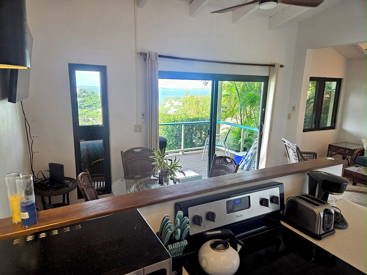 A kitchen with a stove, toaster, and coffee maker. There is a large window with a view of greenery and a balcony.