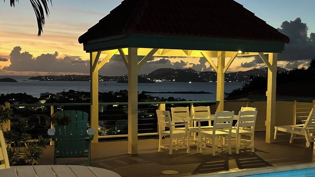 A poolside area with lounge chairs and a gazebo overlooking a body of water at sunset. - Charming Corner Condo with A/C, Stunning Water Views, and Gorgeous Sunsets! (St John)