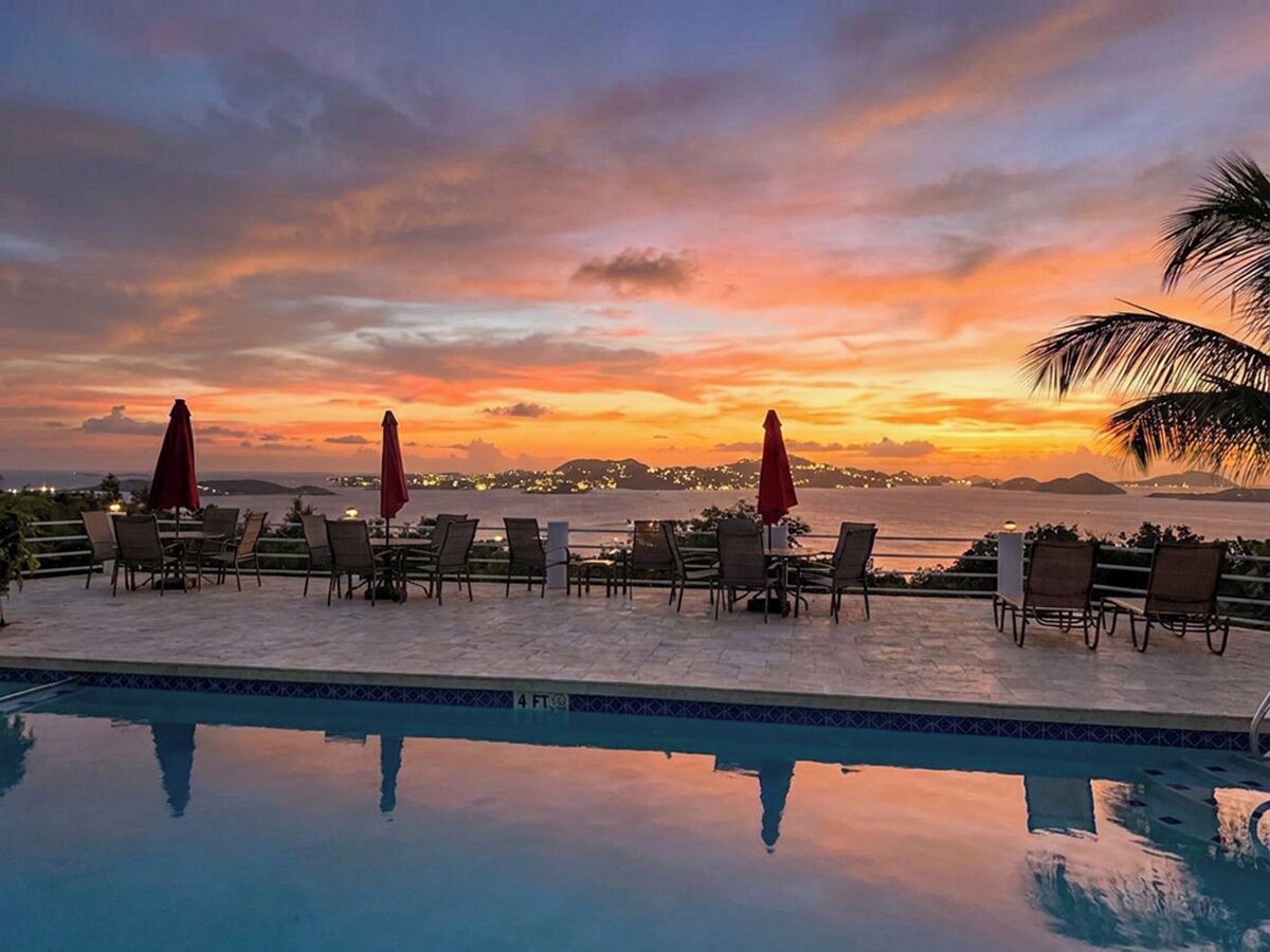 A poolside area with lounge chairs and umbrellas, overlooking a body of water during sunset.