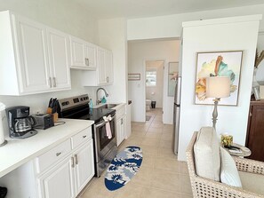 Une cuisine moderne avec des meubles blancs, une machine à café et un grille-pain. Un tapis bleu et blanc recouvre le sol.