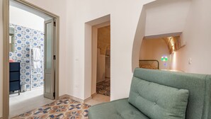 A modern living room with a green sofa, patterned floor tiles, and a door leading to a bathroom with a shower and a towel rack. - Pescamare Apartment Polignano A Mare (Polignano a Mare)