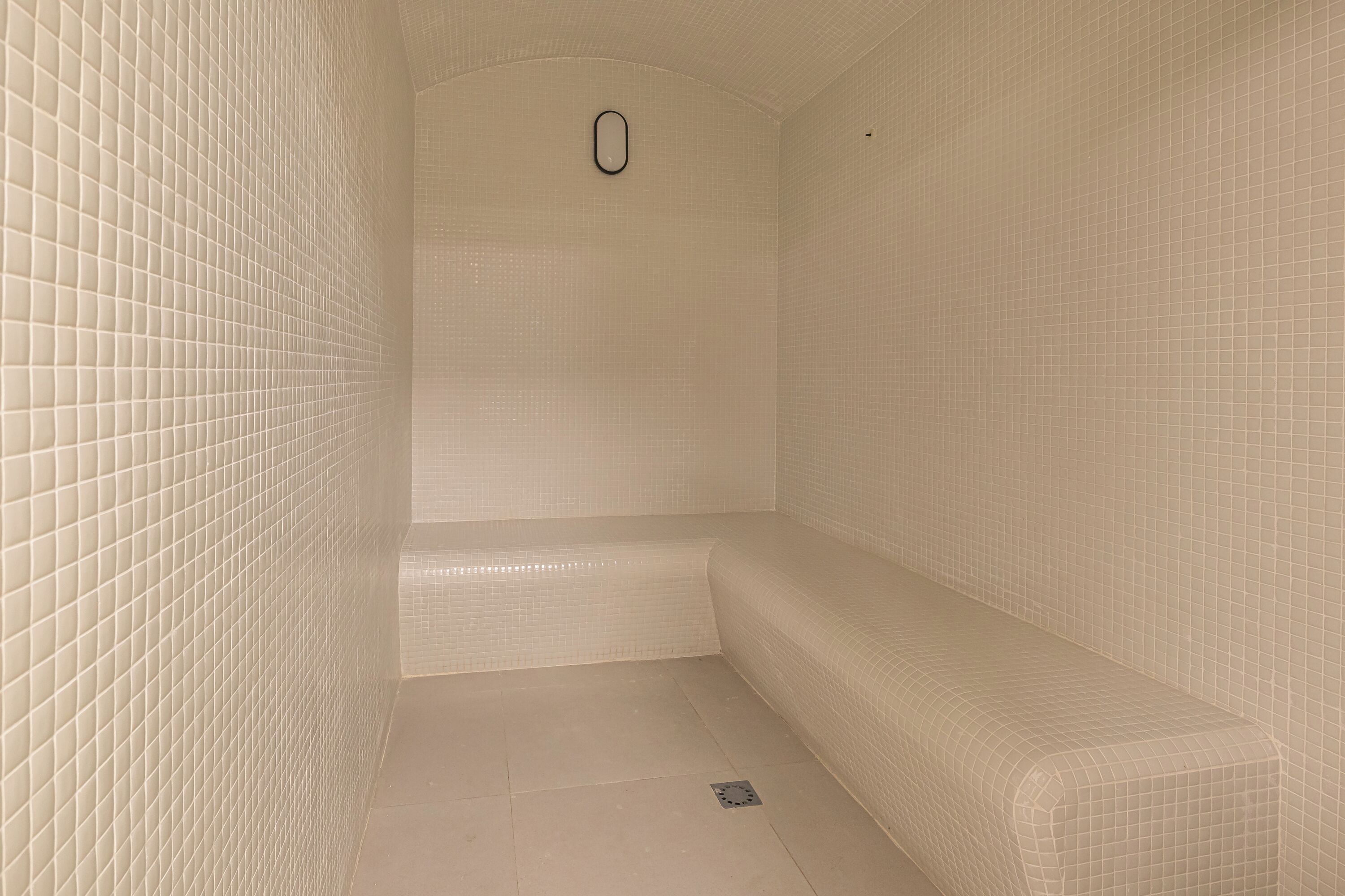 Un cuarto pequeño con azulejos, un banco y un desagüe en el centro.