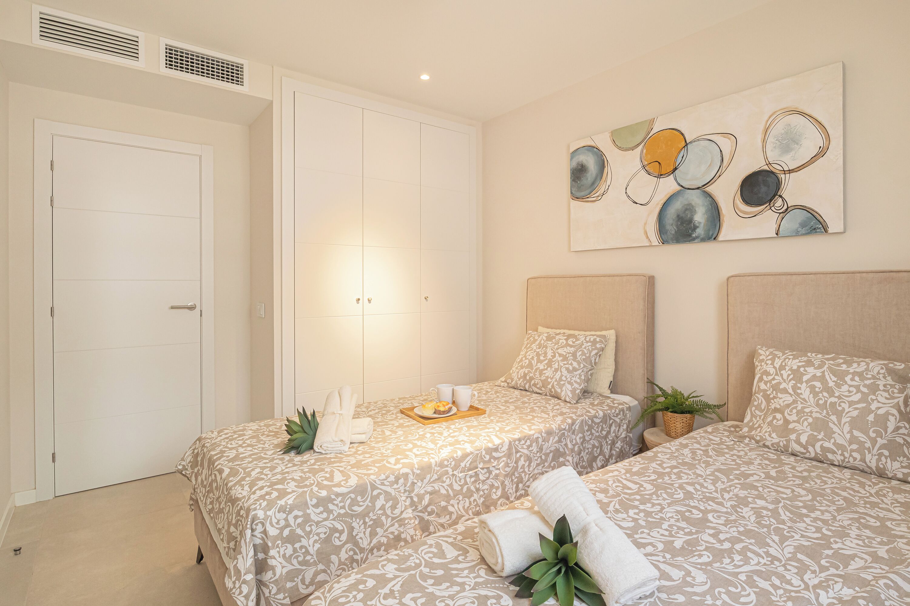 A hotel room with two beds, a large artwork on the wall, and a small plant on the bedside table.