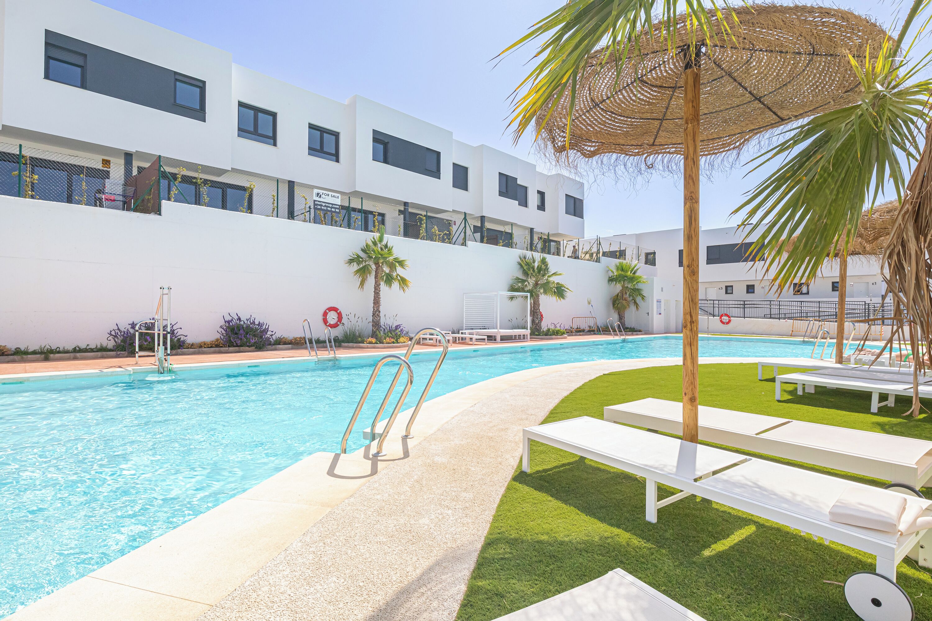 A swimming pool with a clear blue water, surrounded by white lounge chairs and palm trees.