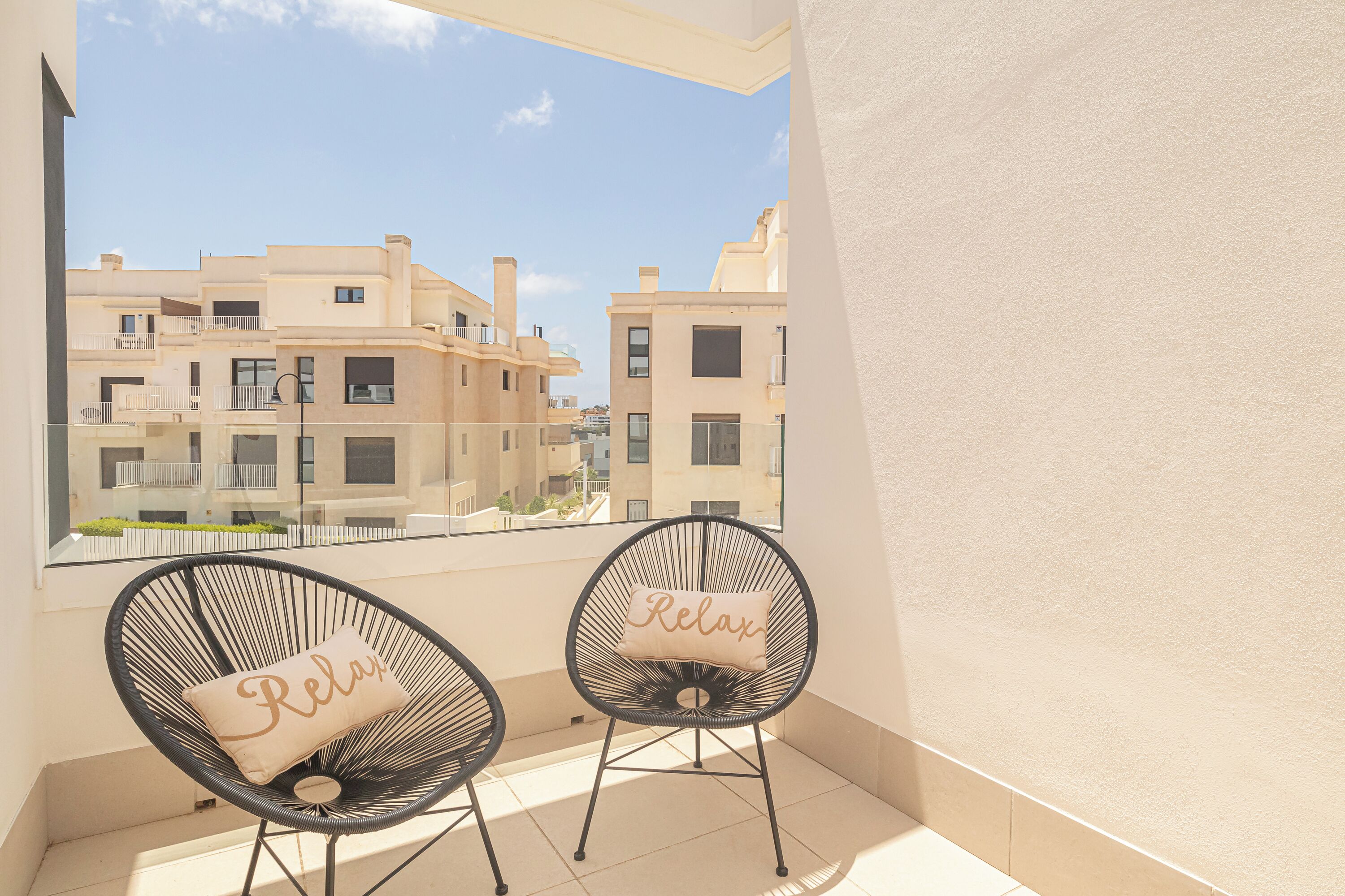 Dos sillas con estructura de alambre negro y cojines color beige en un balcón con vista a edificios residenciales.