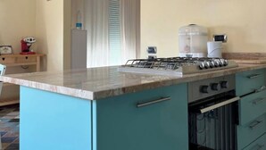 A kitchen with a gas stove, oven, and a glass range hood. There is a water dispenser and a coffee maker on the counter. The cabinets are teal, and the floor has a patterned tile design. - 5 min from the sea large Apartment - Wifi and Air Conditioning (Lido di Camaiore)