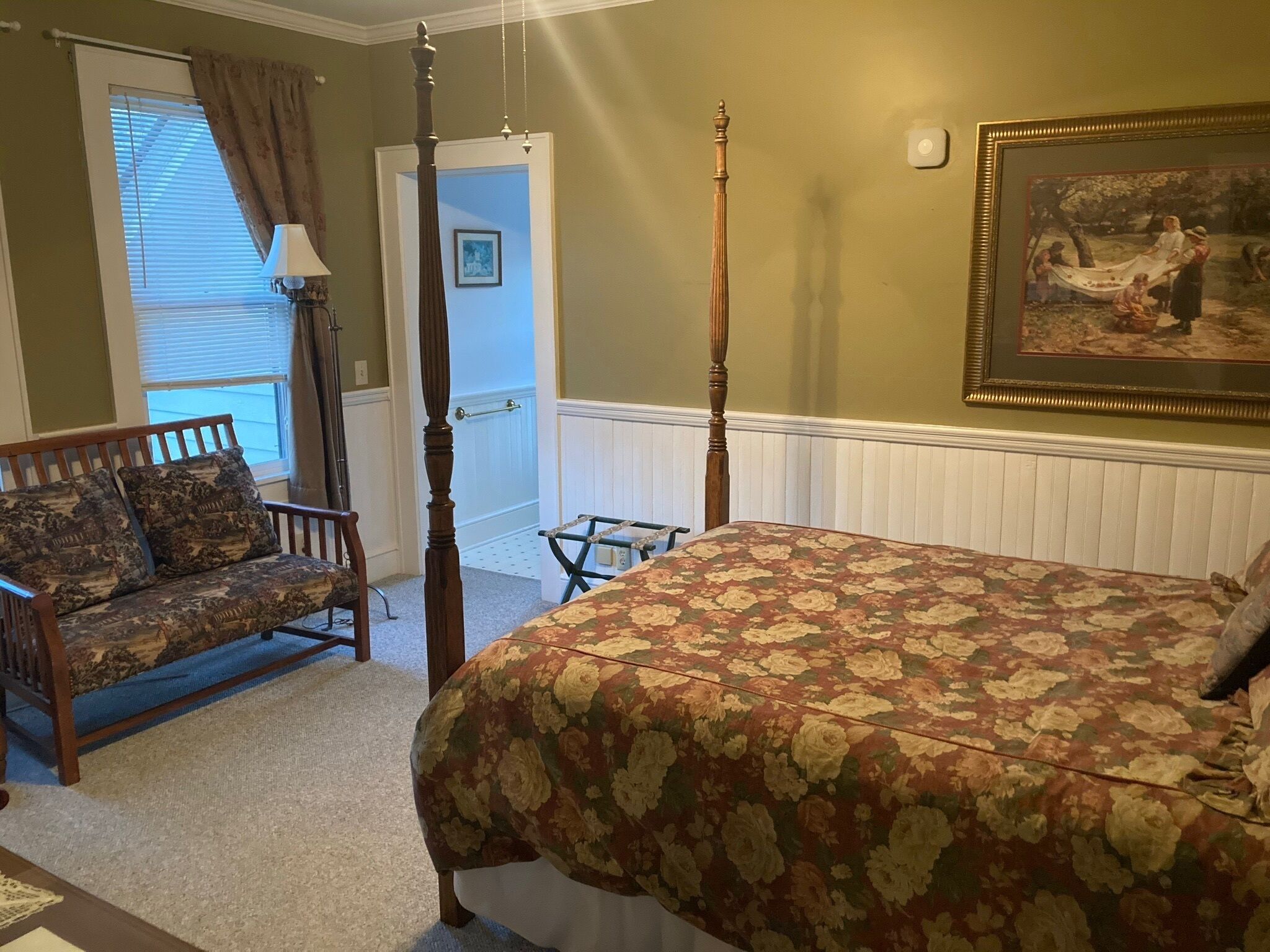 A bedroom with a four-poster bed, a wooden bench, a chair, and a painting on the wall.