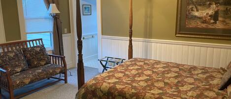A bedroom with a four-poster bed, a wooden bench, a chair, and a painting on the wall.