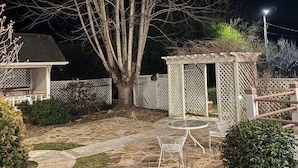 A stone patio with a pergola, a small shed, and a tree. - The Historic Herren House (Waynesville)