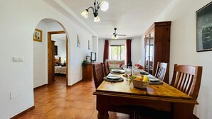 A dining area with a wooden table set for four, surrounded by chairs. There is a ceiling fan above and a window with curtains to the right. - Apartamento La Fuente At Home by At Home Costa del (Frigiliana)
