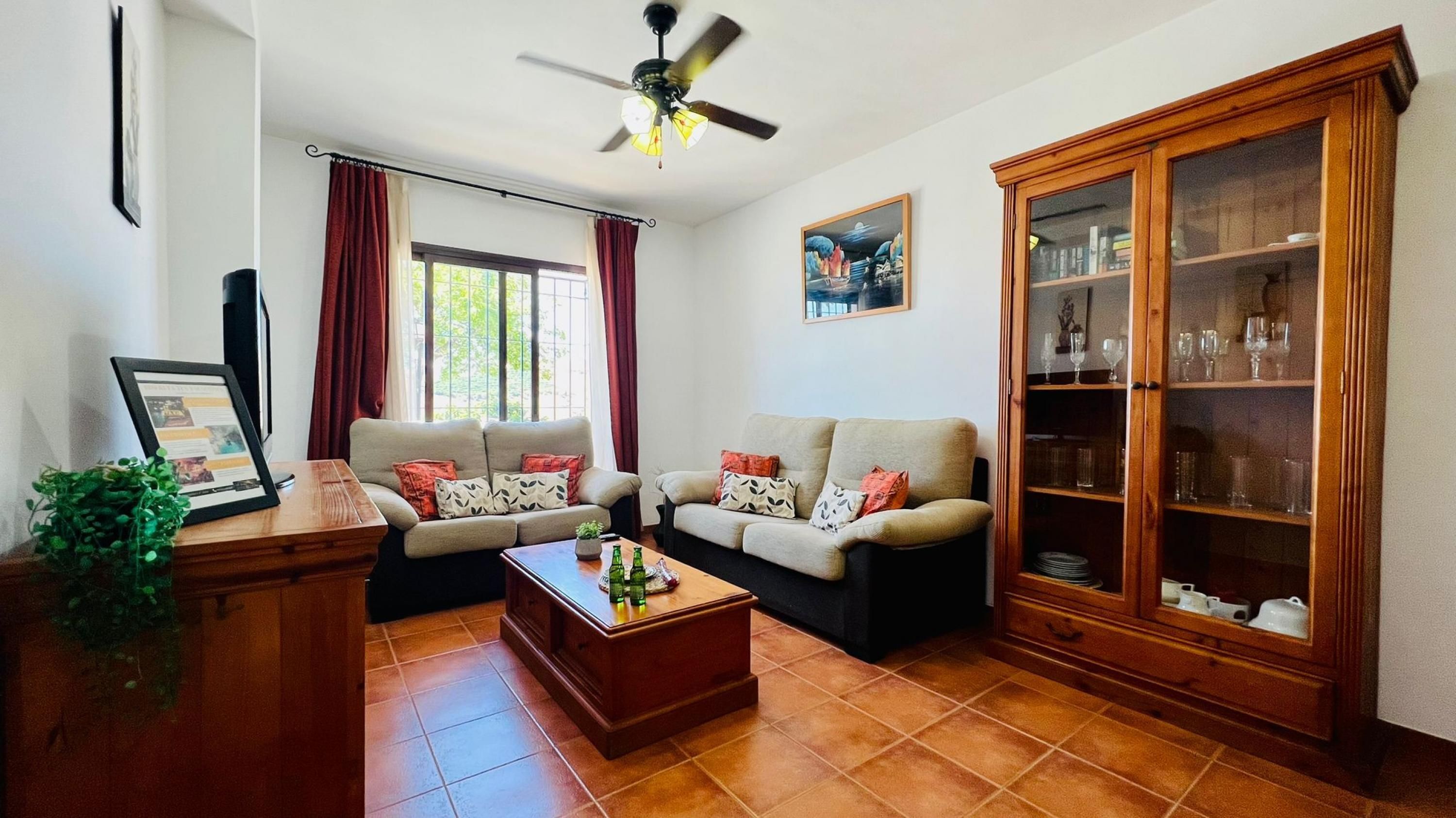 Ein Wohnzimmer mit zwei Sofas, einem Couchtisch, einer Vitrine mit Gläsern und einem Deckenventilator.