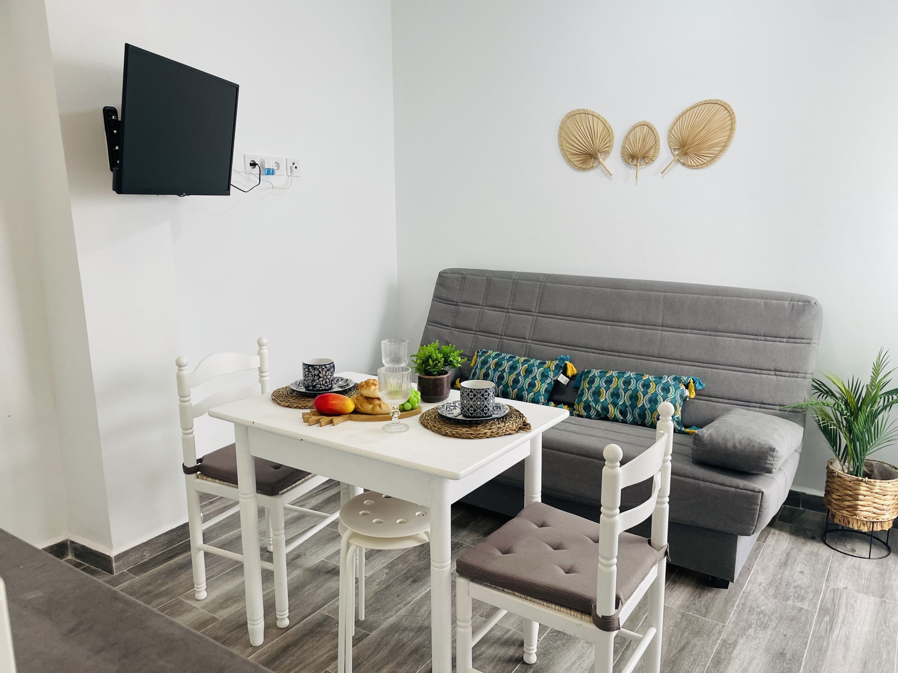 Una sala de estar moderna con una mesa de comedor blanca, sofá gris y televisor de pantalla plana montado.