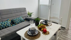 A modern living room with a grey sofa, a white coffee table, and a white chair. There are decorative plates, a glass, and a bowl of fruit on the table. - Apartamento Alboran Panama by At Home Costa del (Nerja)