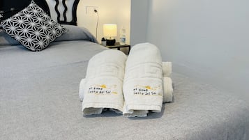 A bed with a geometric patterned pillow, a white towel with text, and a bedside table with a lamp.