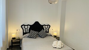 A neatly made bed with a grey bedspread and two patterned pillows, a bedside table with a lamp, and a wall-mounted light fixture. - Apartamento Alboran Panama by At Home Costa del (Nerja)