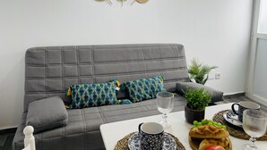 A modern living room with a grey sofa, patterned cushions, a small potted plant, and a dining area with a white table set for two. - Apartamento Alboran Panama by At Home Costa del (Nerja)
