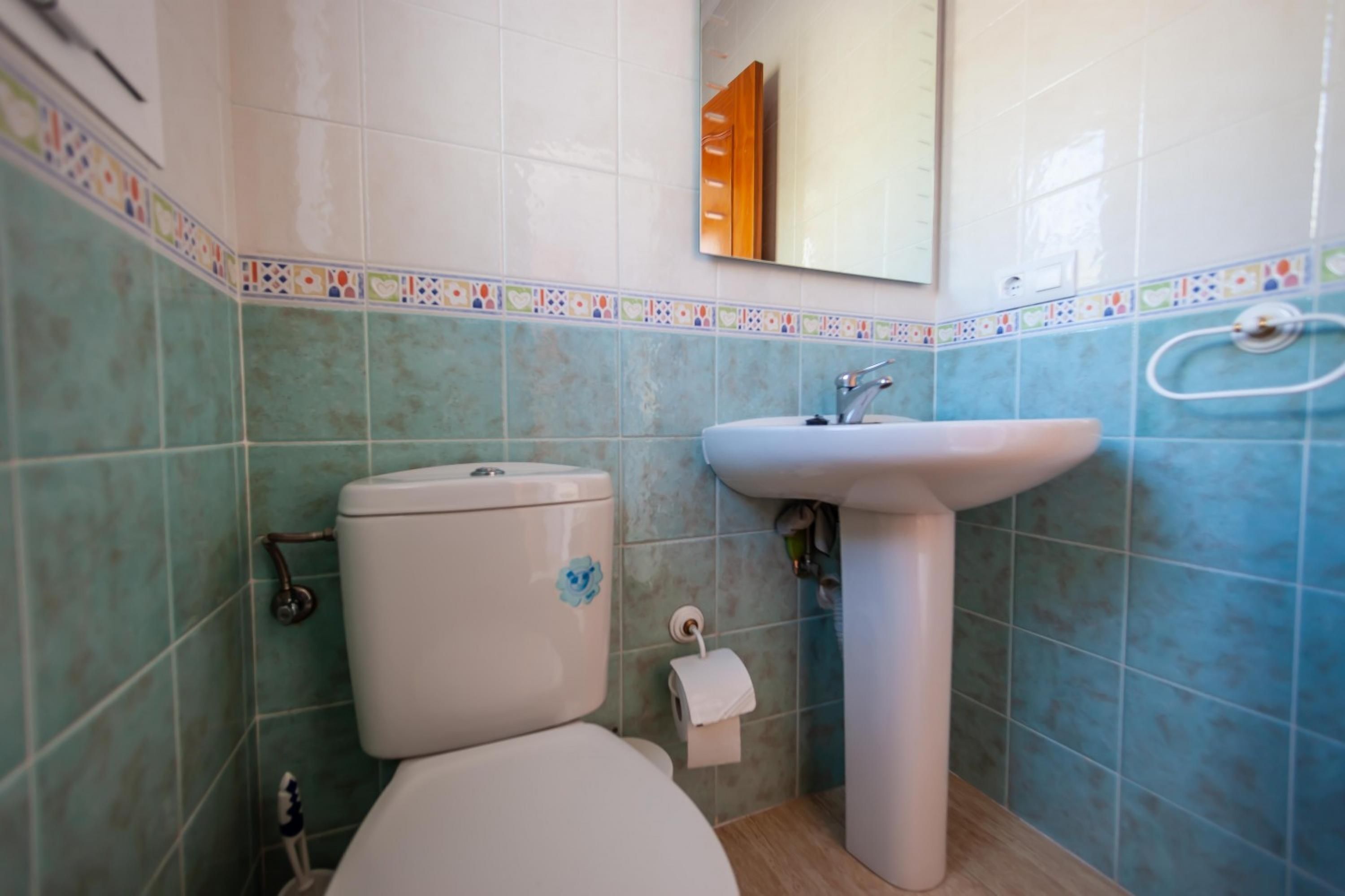 A bathroom with a toilet, sink, and tiled walls.