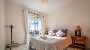 A bedroom with a large bed, two bedside lamps, a nightstand, a window with curtains, and a view of the outdoors.