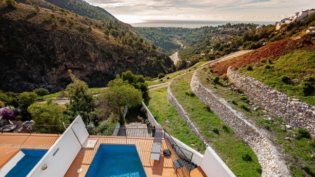 A pool area with a view of a valley and a stone wall.