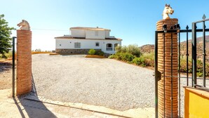A white building with a tiled roof, a gravel driveway, and a gated entrance with horse statues. - Villa Sanchez Sol by At Home Costa del Sol (Torrox)