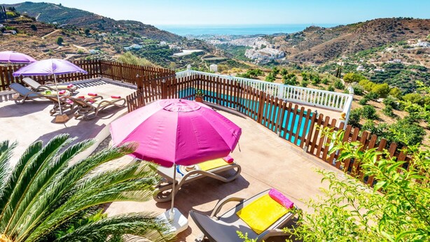 A poolside area with lounge chairs and umbrellas, surrounded by a wooden fence, overlooking a scenic landscape with hills and a view of the sea. - Villa Sanchez Sol by At Home Costa del Sol (Torrox)