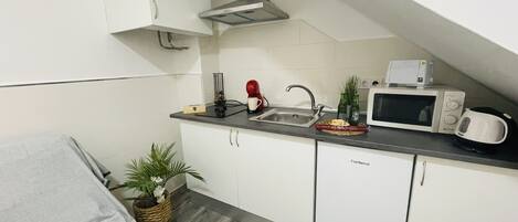 A compact kitchen with white cabinets, a microwave, a coffee maker, and a toaster.