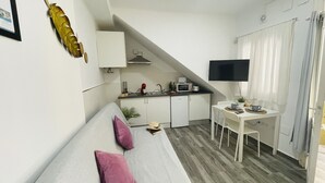 Ein kompakter Raum mit Bett, kleinem Schreibtisch, Küchenzeile und Fernseher.