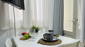 Ein weißer Tisch mit Fernseher, einer Topfpflanze, einer Glasvase, einer Obstschale und einem Satz dekorativer Tassen.