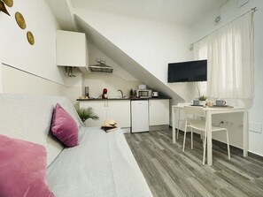 Un espace de vie compact comprenant un coin cuisine, un coin repas et un téléviseur fixé au mur.