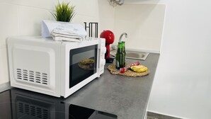 A kitchen with a white microwave, a red kettle, and a sink.
