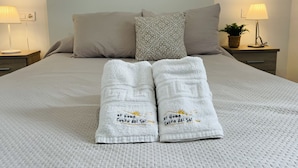 A neatly made bed with two towels, a headboard, and two bedside lamps.